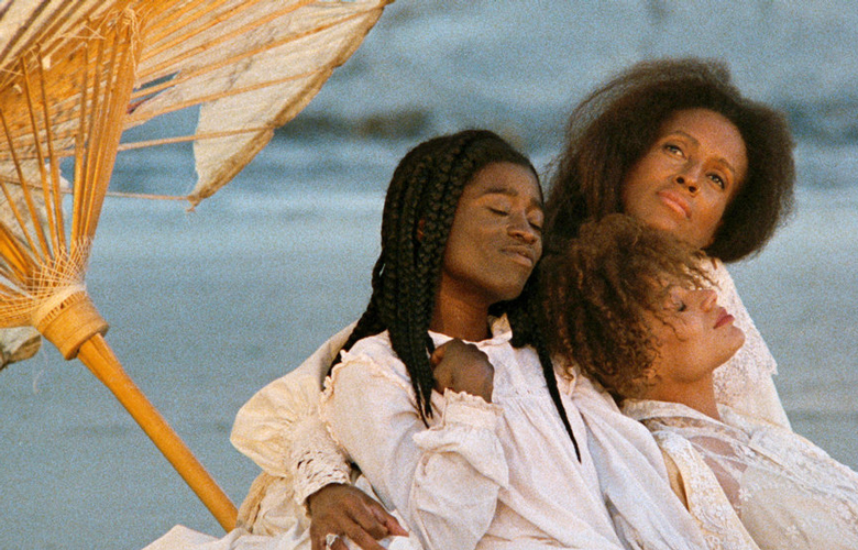 Drei schwarze Frauen am Strand neben einem Strohsonnenschirm, die sehr zufrieden lächeln und ihr Augen geschlossen halten.