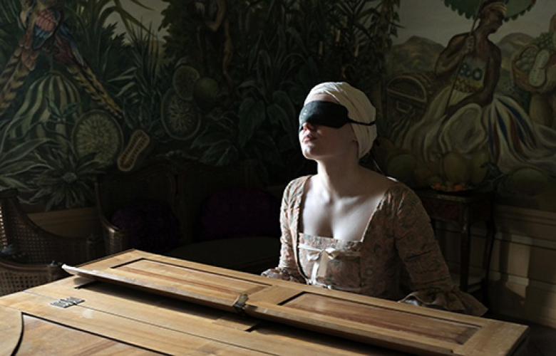 Ein Filmstil aus "Licht": Eine Frau in altem Gewand sitzt mit Augenbinde an einem Klavier.